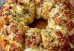 Cheesy ham bread ring baked golden brown, topped with melted cheese and herbs