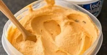 Creamy pumpkin cheesecake mousse in a glass container with a wooden spoon