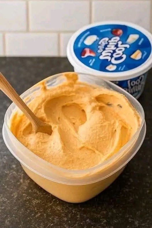 Creamy pumpkin cheesecake mousse in a glass container with a wooden spoon